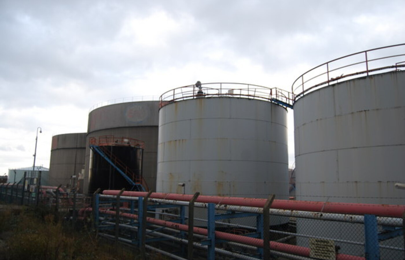 Insulated industrial liquid storage tanks with metallic cladding and steam piping